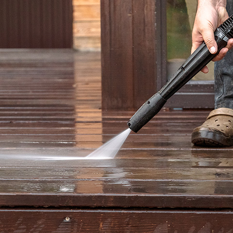 Person pressure washing a wooden deck, with icon of a power washer representing E3’s pressure washing service.