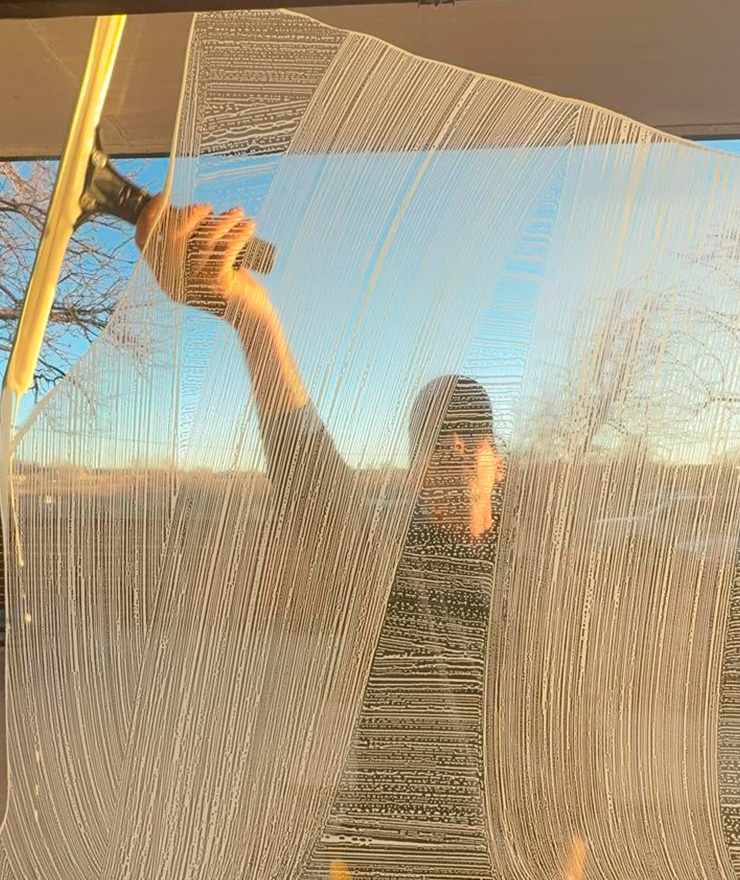 Professional window cleaner scrubbing a large glass panel with soap and sponge at sunset in Lafayette, Colorado.